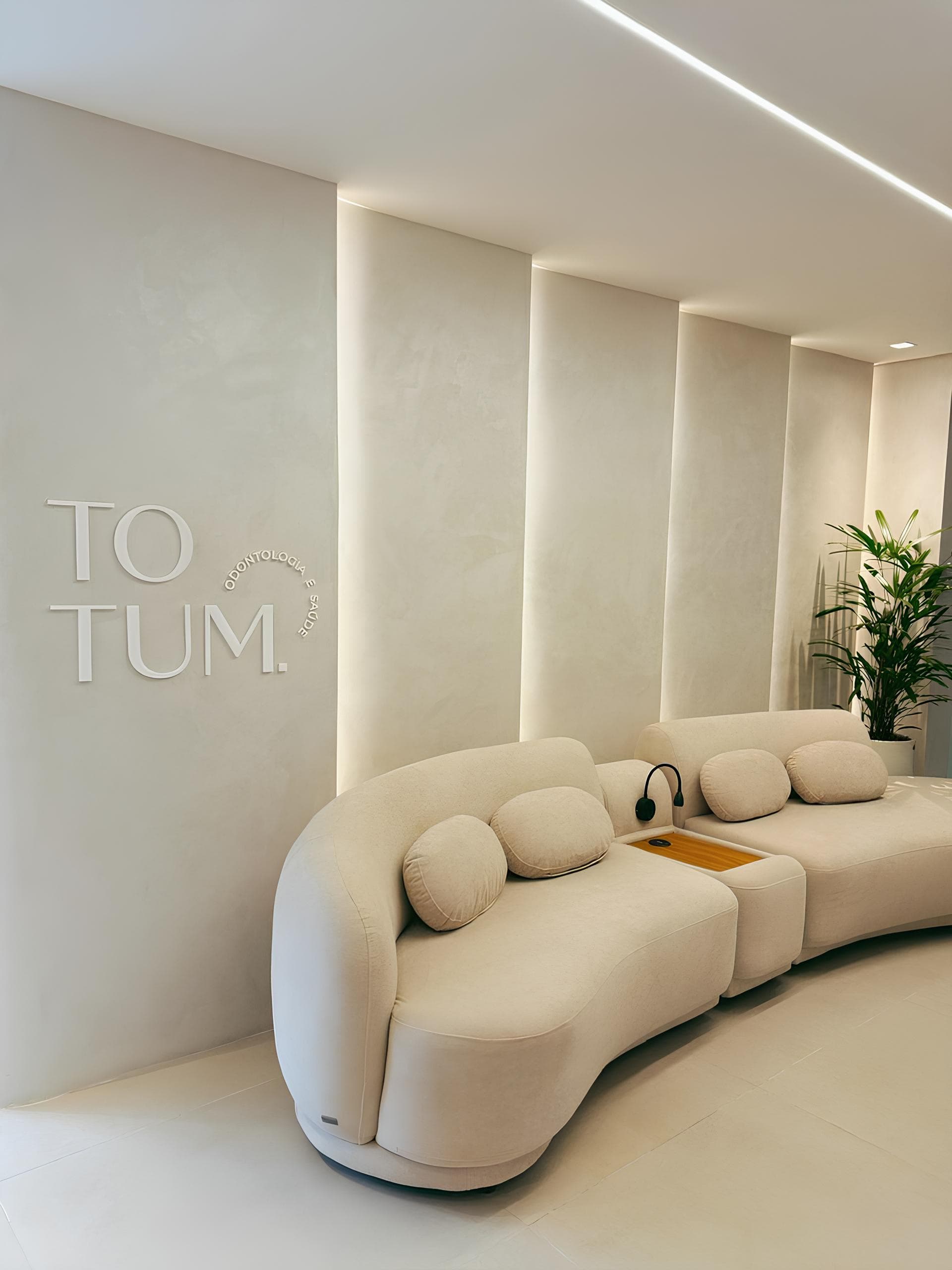 Recepção da Totum Odontologia com sofá bege e logo na parede